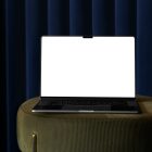 Front view, blank MacBook Pro Device Mockups laying on the bottle green pouf with gold elements against a deep blue curtain in the background.