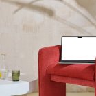 Front view, blank MacBook Pro Device Mockups laying on the red armchair against a wall in the background.