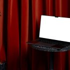 Front view, blank MacBook Pro Mockup standing on the marble chair against a deep red curtain in the background.
