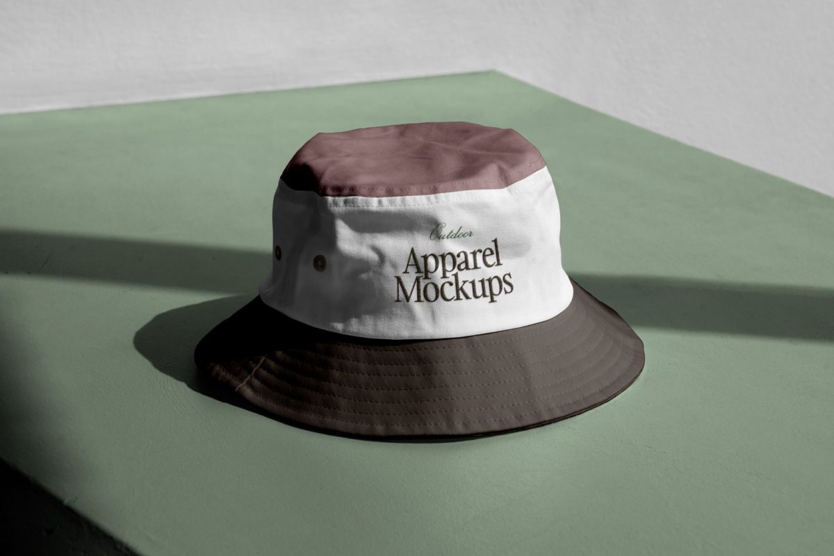 Front view, Bucket Hat Mockup in three colors. Dark brown peak, white, and burgundy laying on the green concrete against white wall.