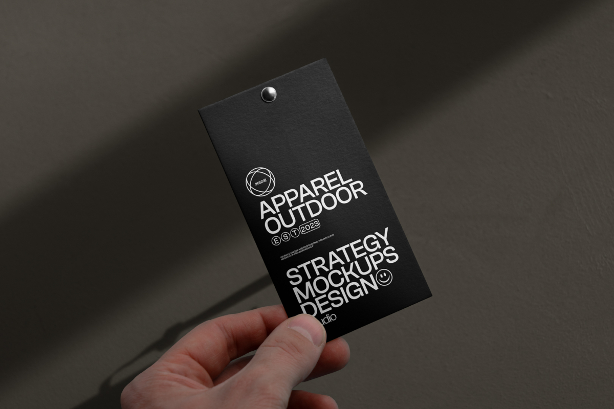 Front view, black label mockup with white typographic design in men's left hand against a dark beige wall.
