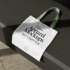 Seen from above, White Canvas Bag Mockup with green handle laying on the dark beige concrete against the marble floor.