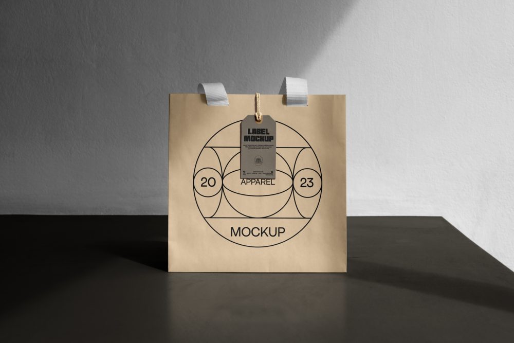 Front view, creamy color Paper Bag Mockup with white handle and craft figure label standing on the dark beige concrete against the white wall.