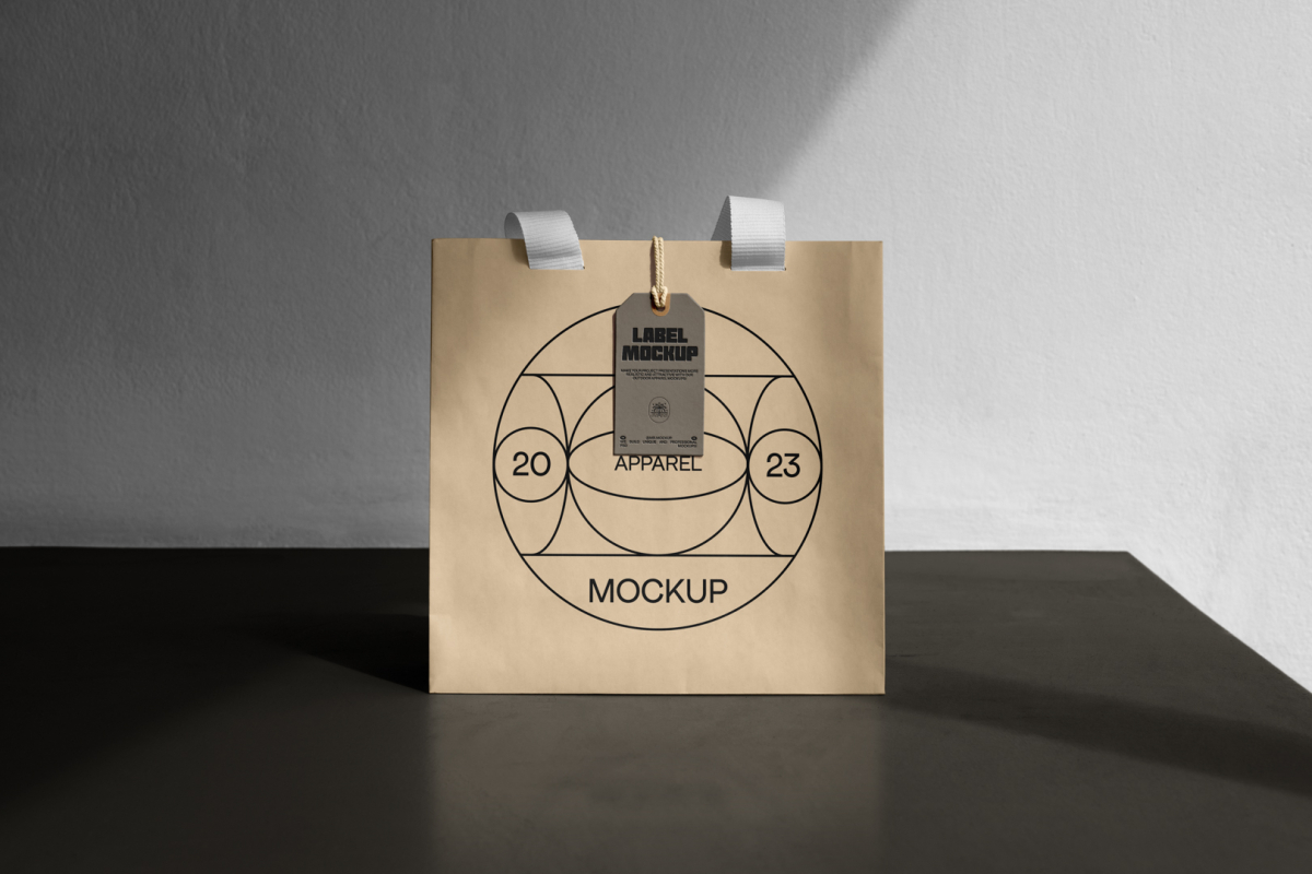 Front view, creamy color Paper Bag Mockup with white handle and craft figure label standing on the dark beige concrete against the white wall.