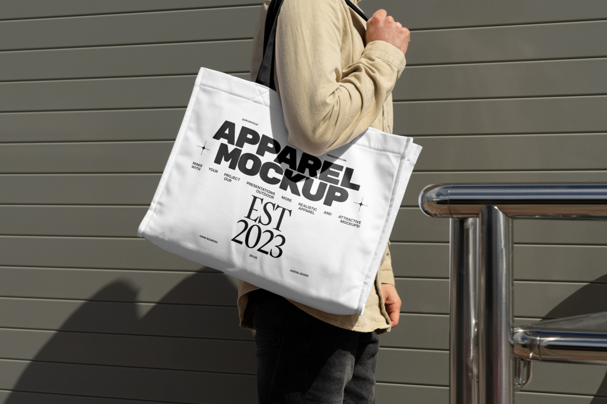 Front view, Men wearing a White Canvas Bag Mockup with a black handle and design on it against rotten green color wall.
