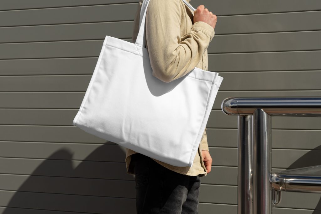 Front view, Men wearing a White Canvas Bag Mockup against rotten green color wall.