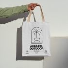 Front view, arm holding a white Canvas Bag Mockup with creamy handle and black typographic design on it against on the white wall.