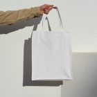 Front view, arm holding a White Canvas Bag Mockup against on the white wall.