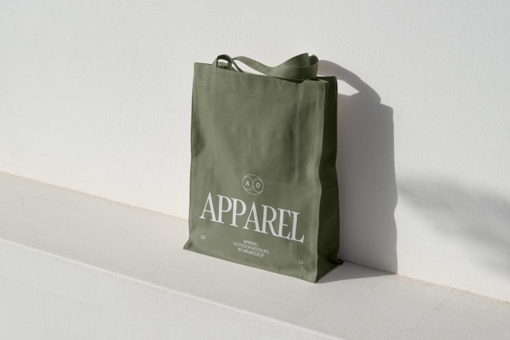 Seen from above, Green Big Canvas Bag Mockup with white typographic design on it standing on the white concrete against white textured wall.