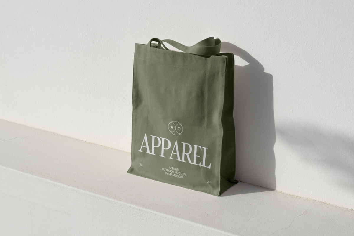 Seen from above, Green Big Canvas Bag Mockup with white typographic design on it standing on the white concrete against white textured wall.