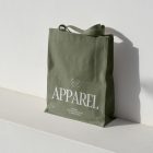 Seen from above, Green Big Canvas Bag Mockup with white typographic design on it standing on the white concrete against white textured wall.