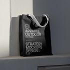 Front view, Black Canvas Bag Mockup with white handle and white typographic design standing on the white windowsill against on the white wall in shadow.