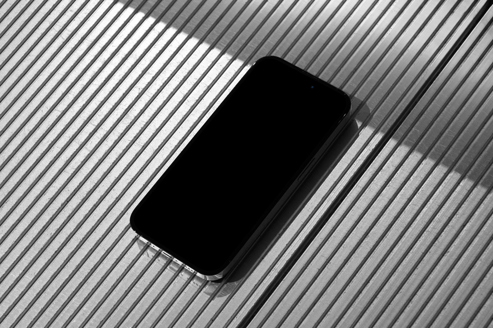 Seen from above, Blank iPhone 14 Pro Mockup laying on the silver plastic panel background.