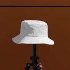 Front view, White Bucket Hat Mockup is mounted on a black tripod against on the dark brown wall.