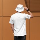 Front view, a man with his back turned, wearing a White T-shirt Mockup and White Bucket Hat Mockup standing against on the gold wall.