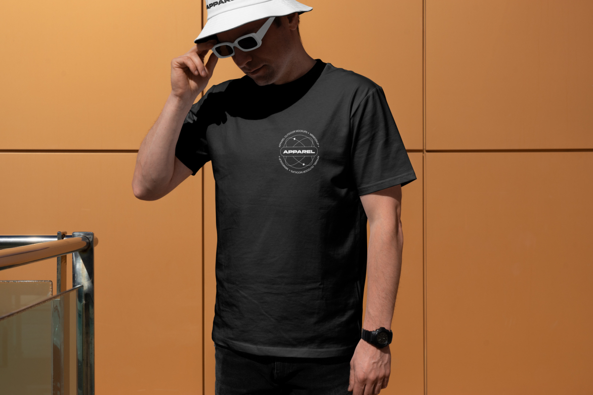 Front view, a man wearing a white black T-shirt Mockup and a white Bucket Hat Mockup standing against on the gold wall.