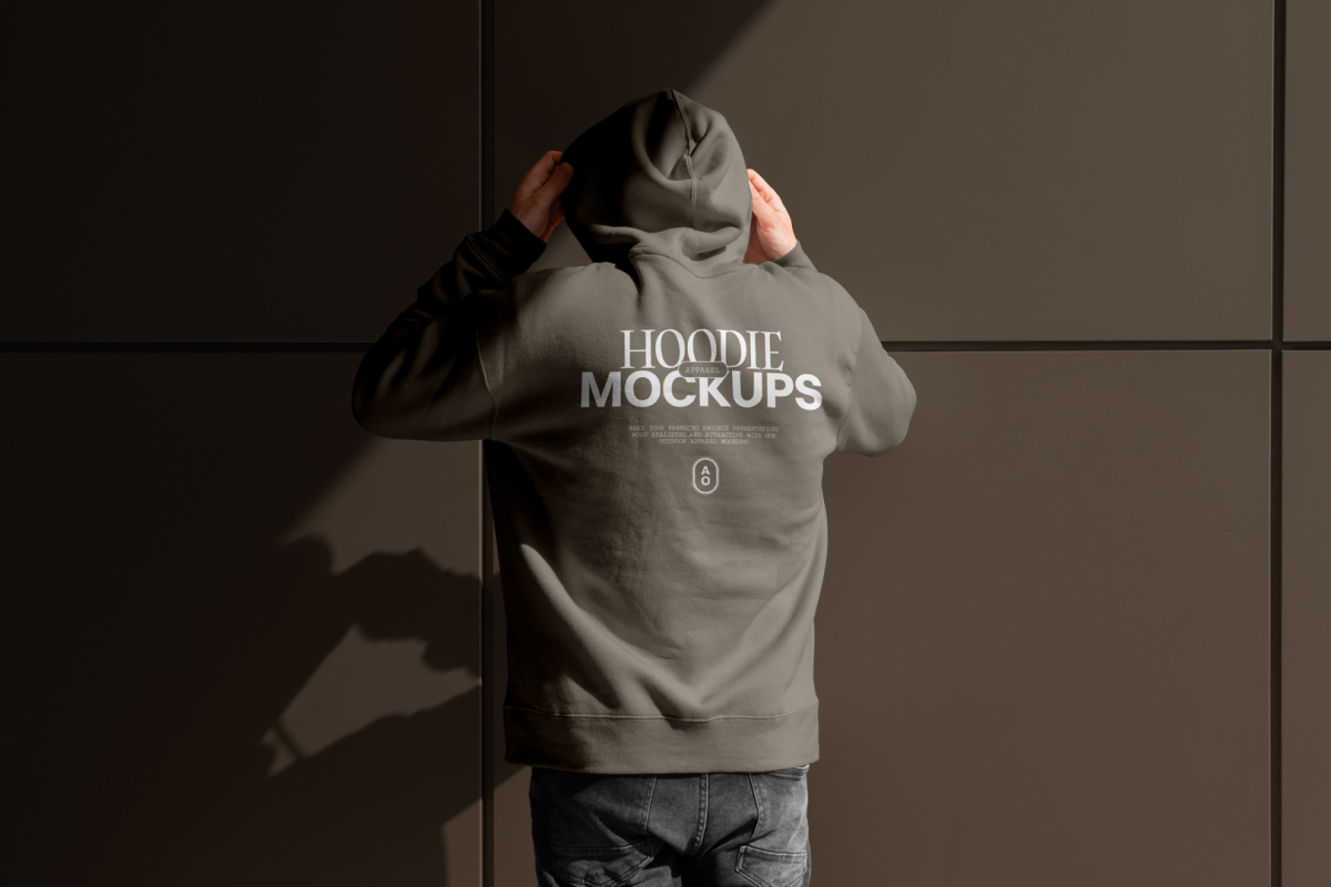 Front view, a man with his back turned, wearing a white gray Hoodie Mockup standing against on the dark gray wall.