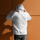 Front view, a man with his back turned, wearing a White Hoodie Mockup standing against on the gold wall.