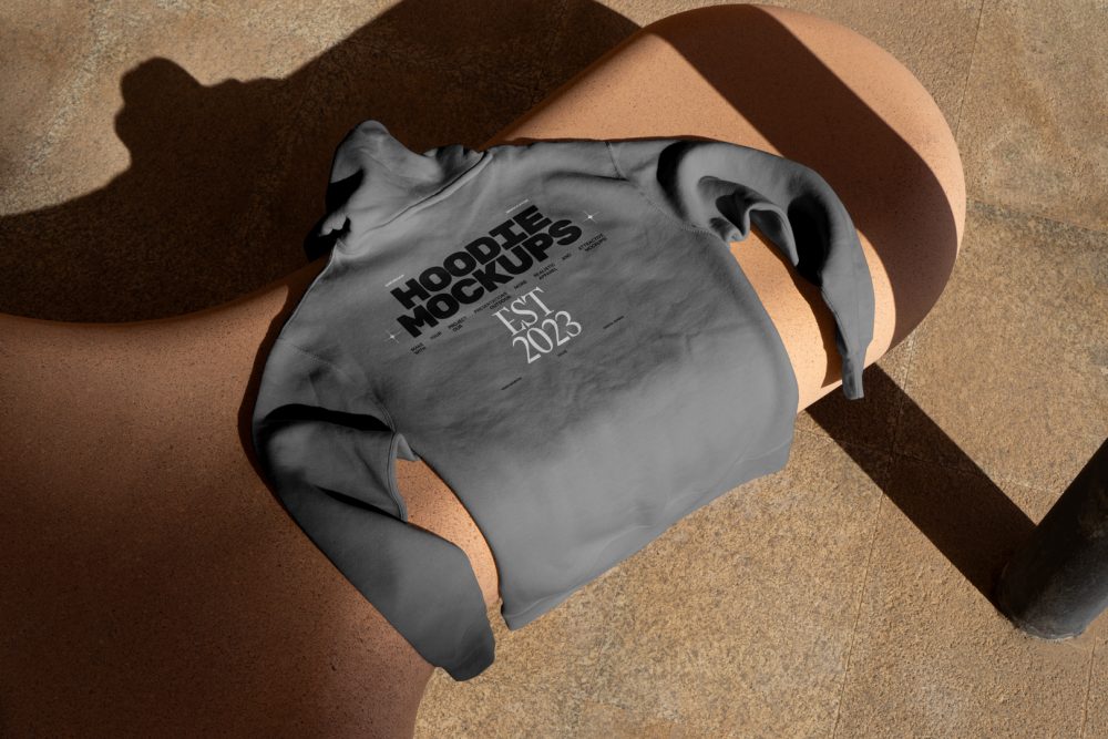 Seen from above, a gray Hoodie Mockup with a black and white typographic design on it laying on the creamy bench against the marble street.