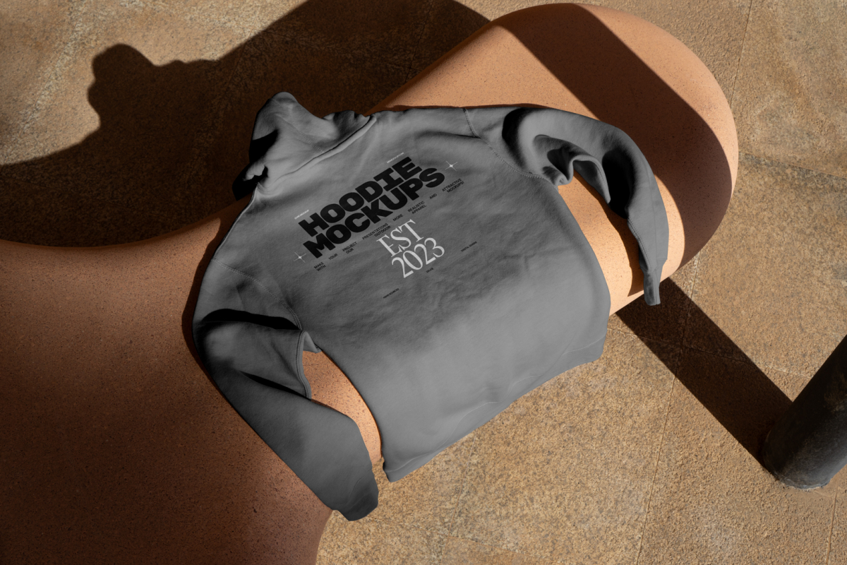 Seen from above, a gray Hoodie Mockup with a black and white typographic design on it laying on the creamy bench against the marble street.