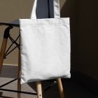 Front view, White Canvas Bag Mockup hanging on the chair against gold wall.