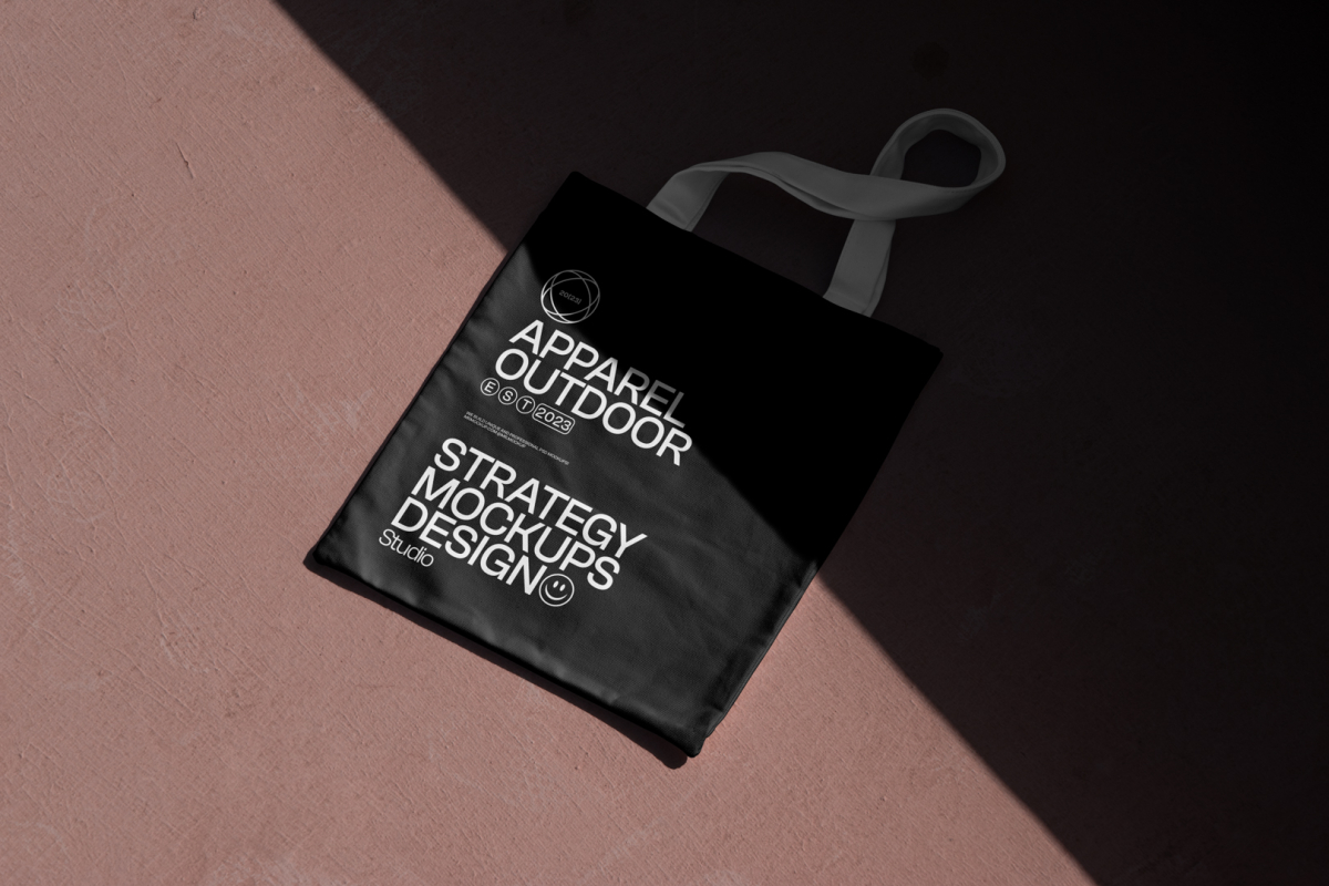 Seen from above, a black Canvas Bag Mockup with a white handle and white typographic design on it laying on the burgundy floor.