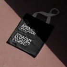 Seen from above, a black Canvas Bag Mockup with a white handle and white typographic design on it laying on the burgundy floor.