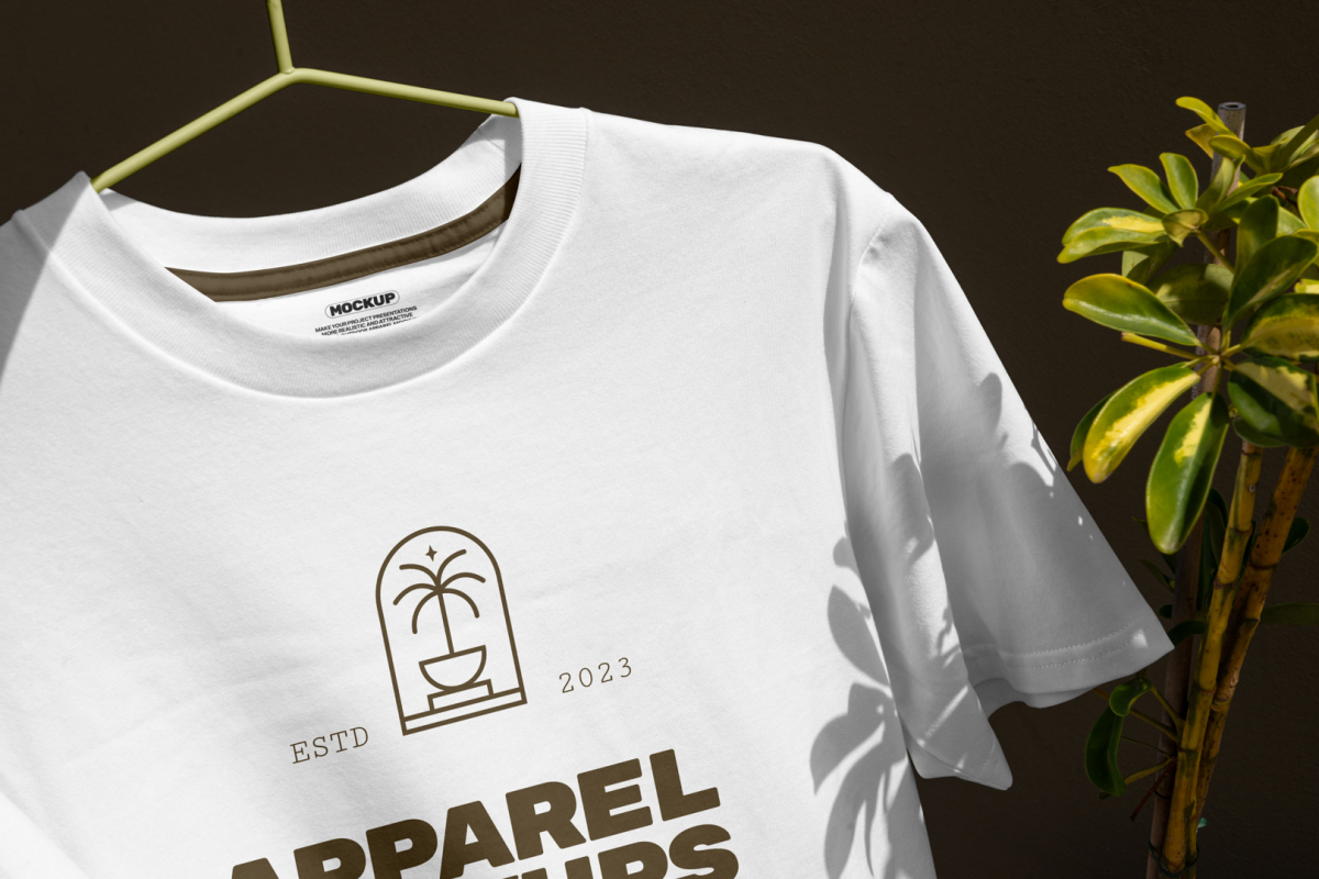 Front view, White T-Shirt Mockup hanging on a lime hanger and gold typographic design on it against a dark brown wall and monster flower.
