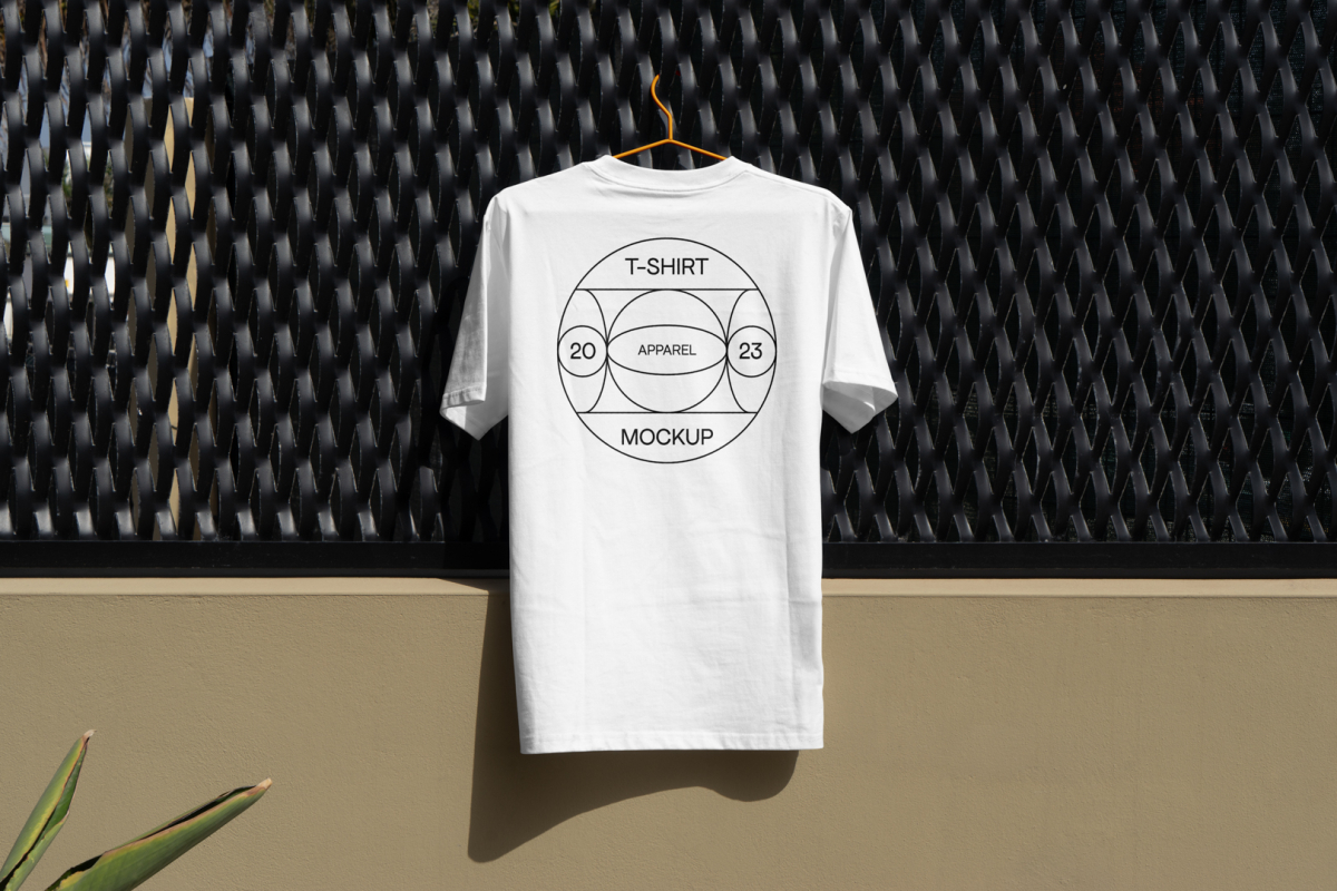 Front view, white T-Shirt Mockup with a black typographic logo on it hanging on an orange hanger attached to a black fence.