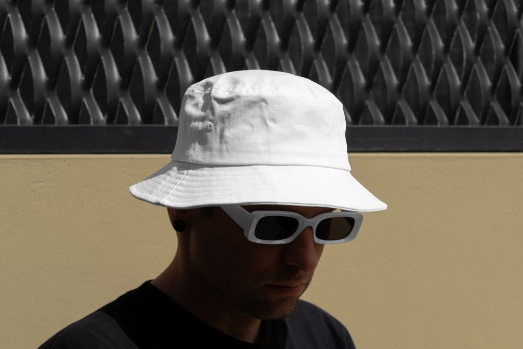 Front view, Men wearing a White Bucket Hat Mockup against a black fence.
