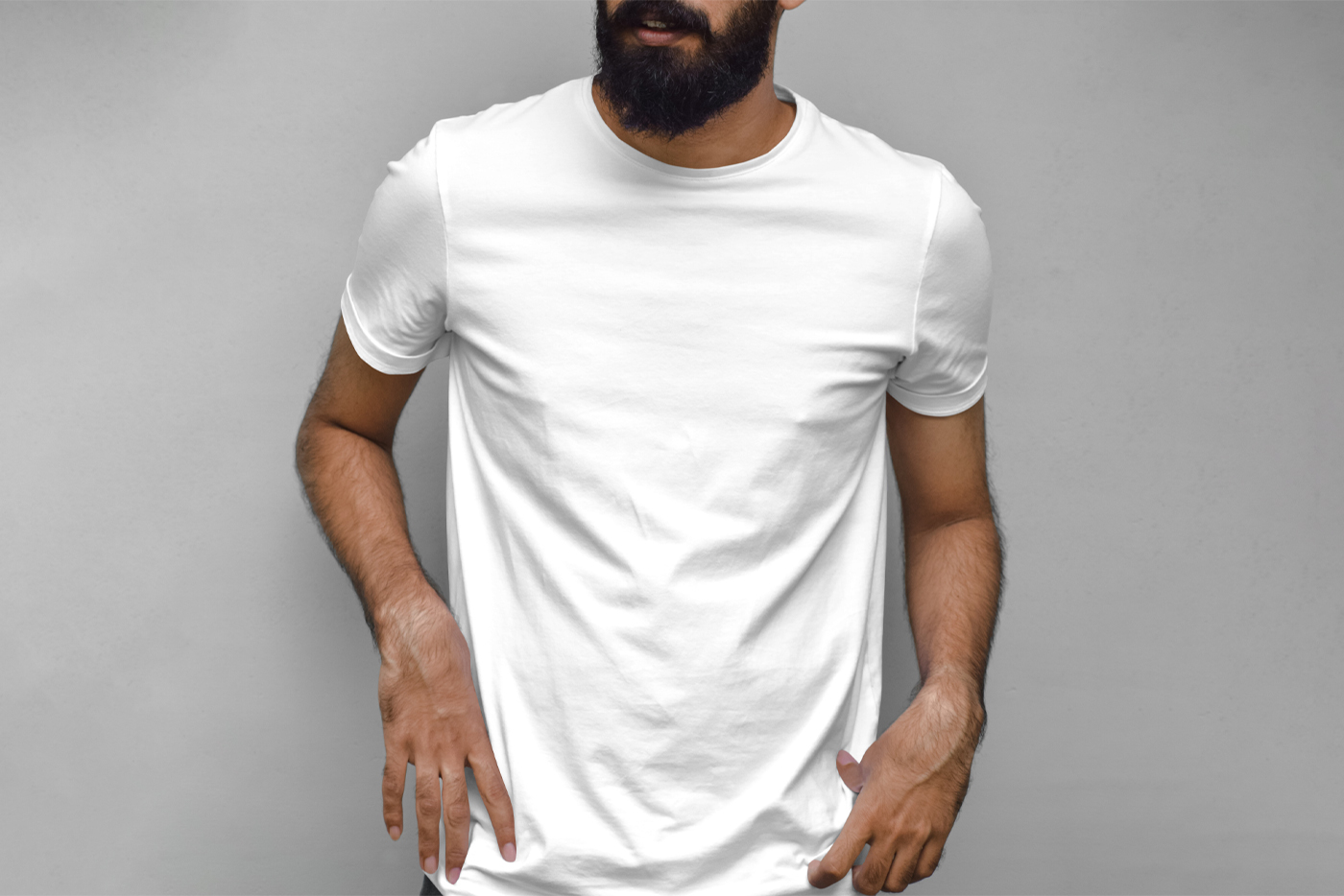 Standing men wearing white t-shirt in front of the gray wall.