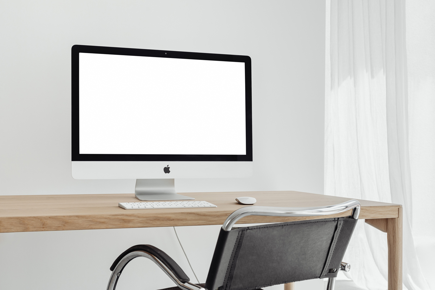 Front view, silver iMac Pro Mockup with white screen standing on the wooden desk in front of the white wall.
