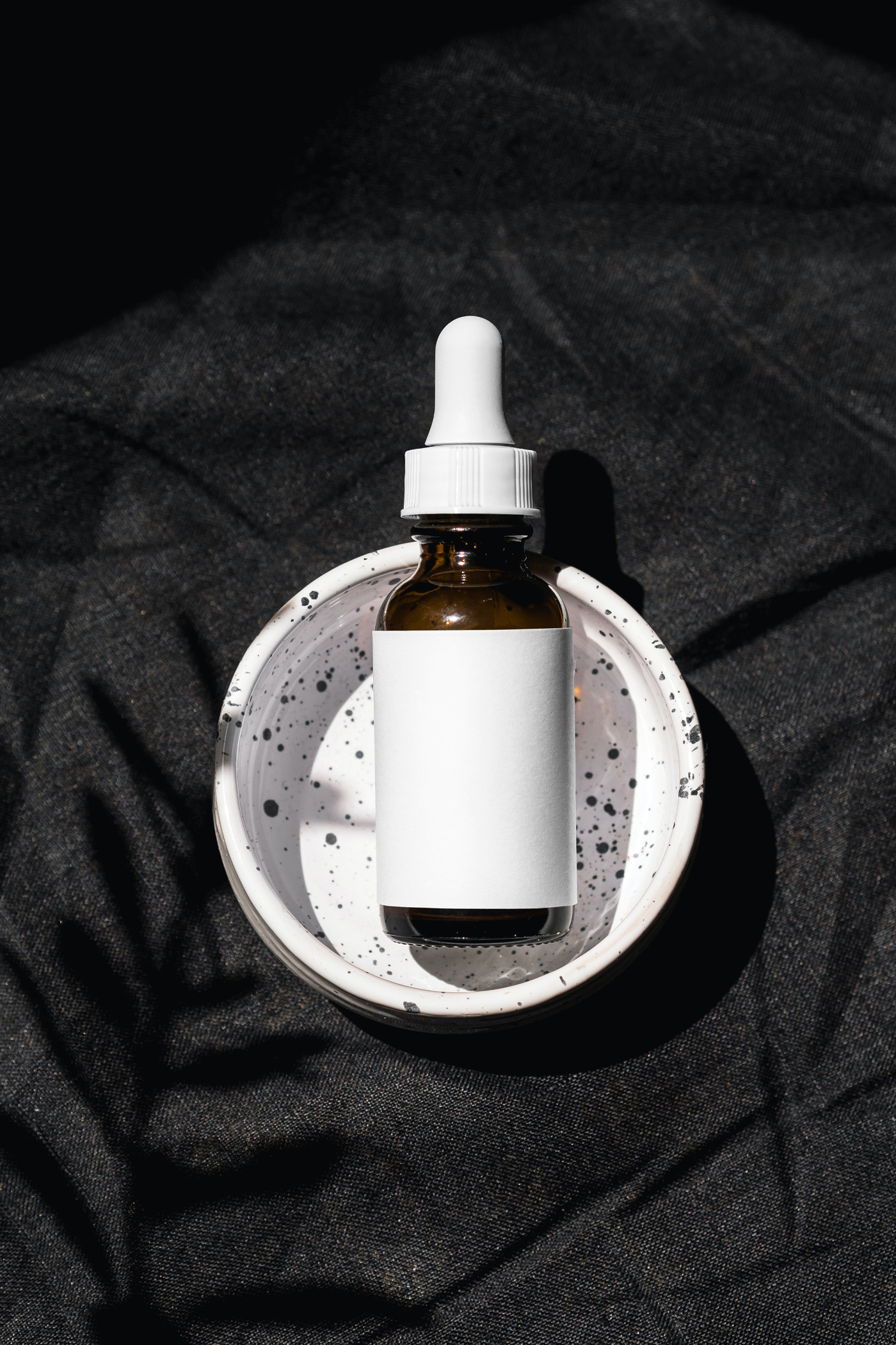 View from above, cosmetic bottle mockup with white label laying it's in the terrazzo ashtray.
