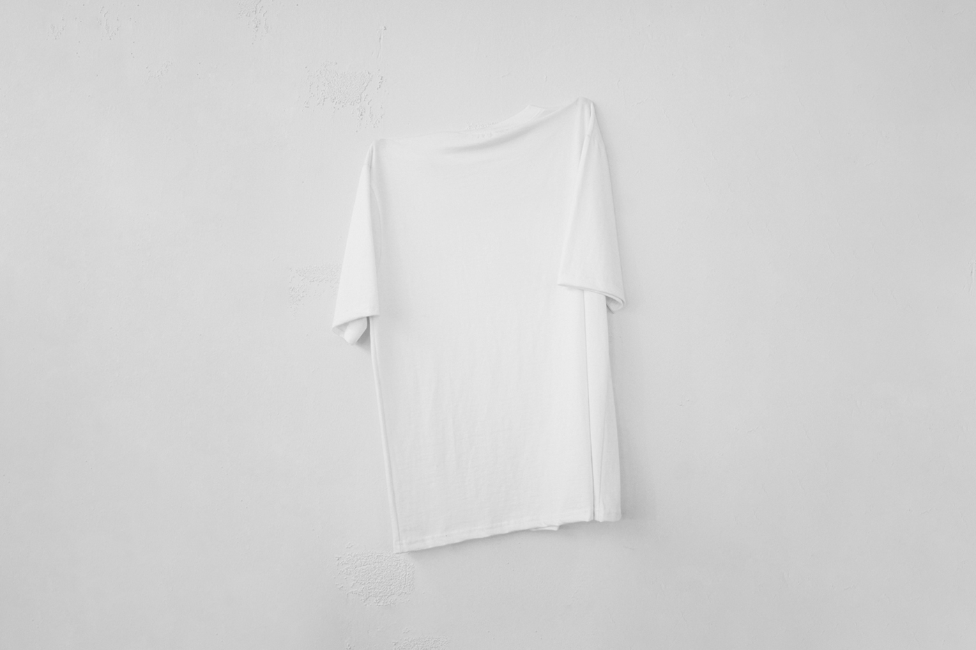 Front view, hanging blank t-shirt mockup on a white wall.