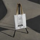 White canvas bag with yellow handle hanging on black tripod.