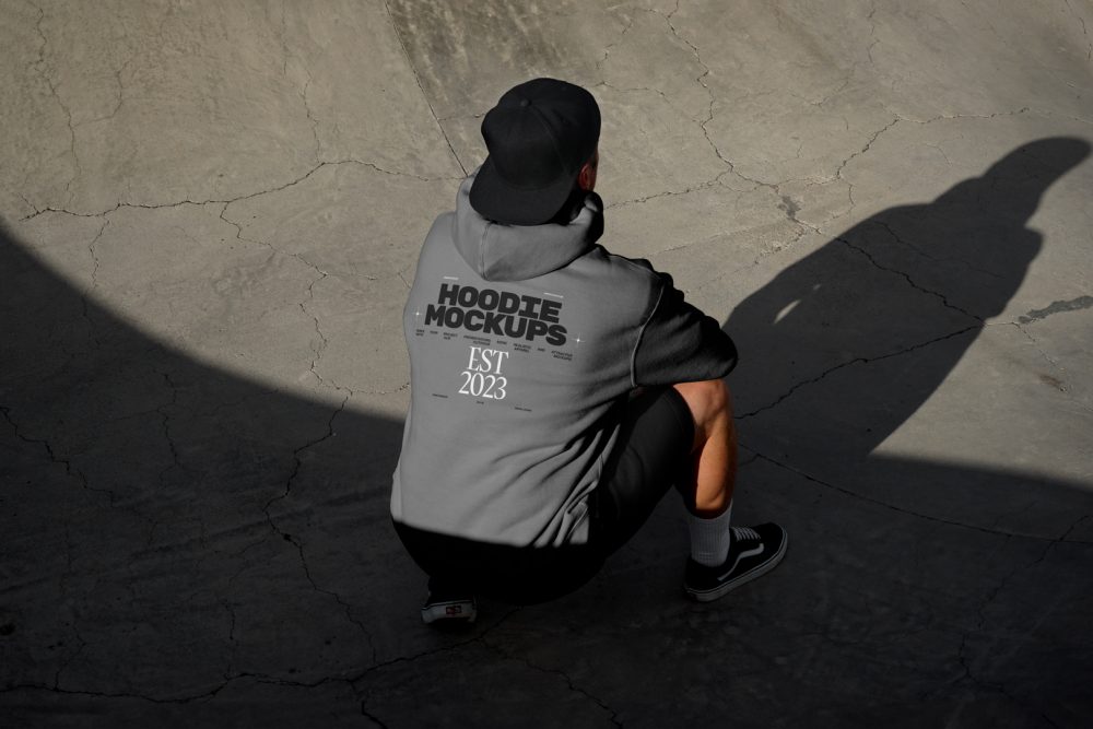 Man wearing dark grey hoodie and black cap on the concrete skatepark.