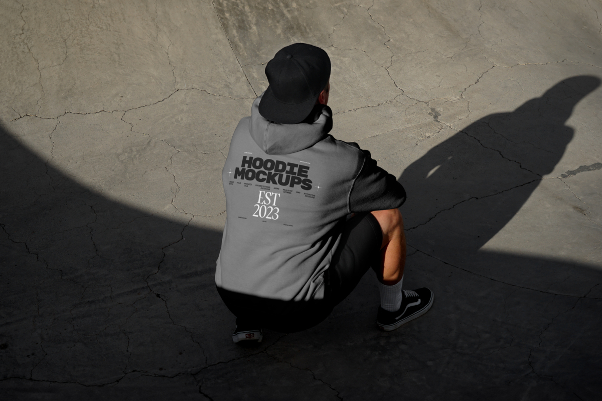 Man wearing dark grey hoodie and black cap on the concrete skatepark.