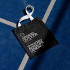 Black canvas bag with white handle laying on blue court.