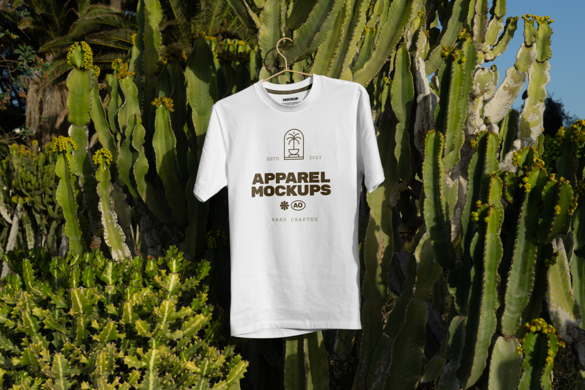 White t-shirt with brown typographic design hanging on the cactus.