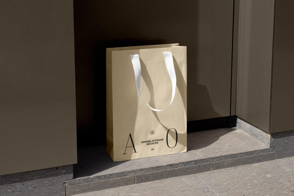 Yellow paper bag with typographic design and white handle in front of brown wall.