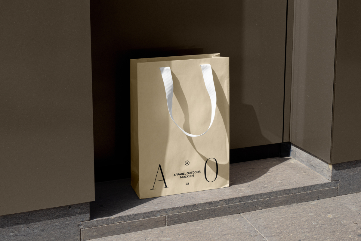 Yellow paper bag with typographic design and white handle in front of brown wall.