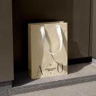Yellow paper bag with typographic design and white handle in front of brown wall.