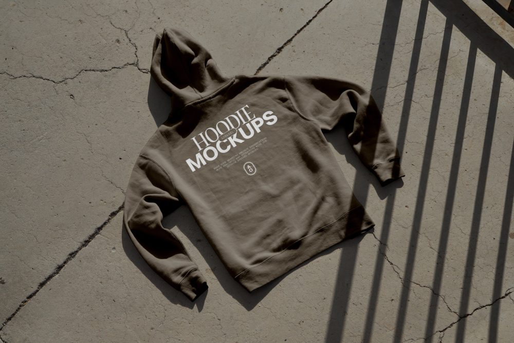 Brown hoodie with white typographic design laying on the concrete ground.