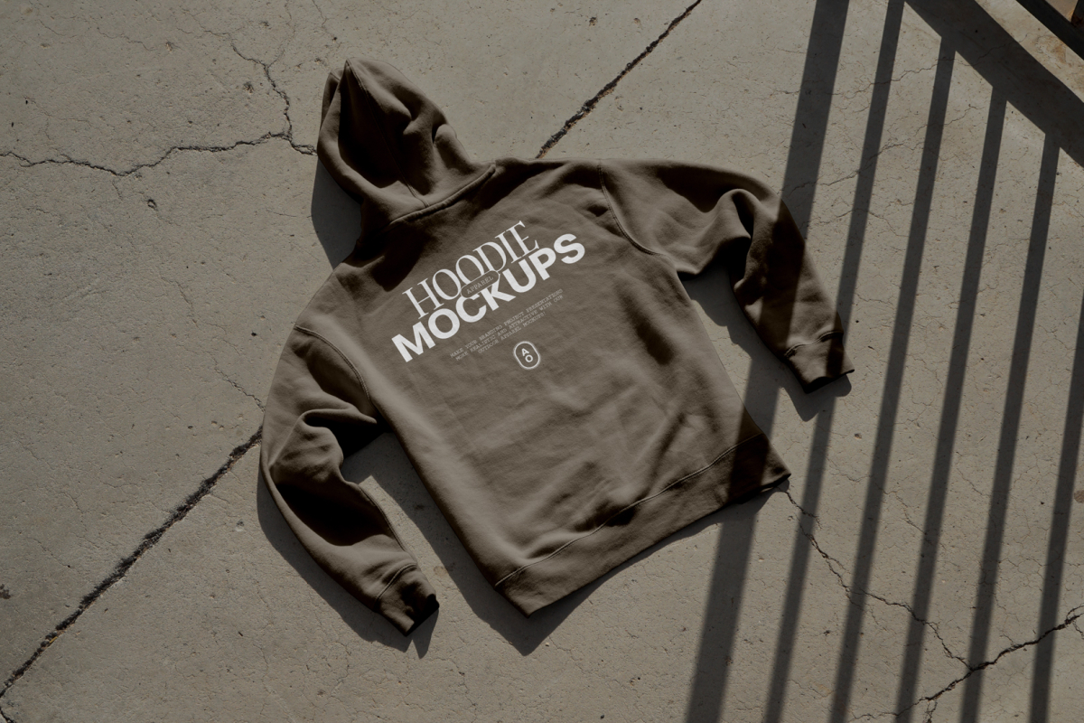 Brown hoodie with white typographic design laying on the concrete ground.