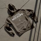 Brown hoodie with white typographic design laying on the concrete ground.