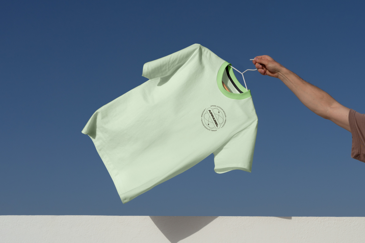 Man holding green t-shirt in front of blue sky.