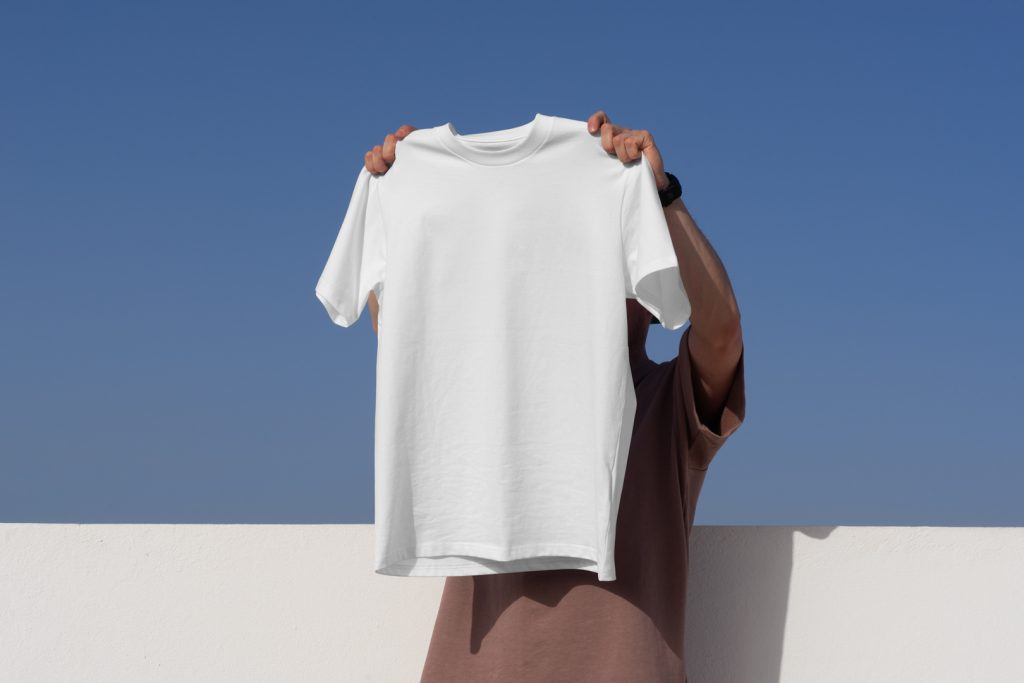 Man holding t-shirt in front of blue sky from outdoor apparel mockups vol.2.