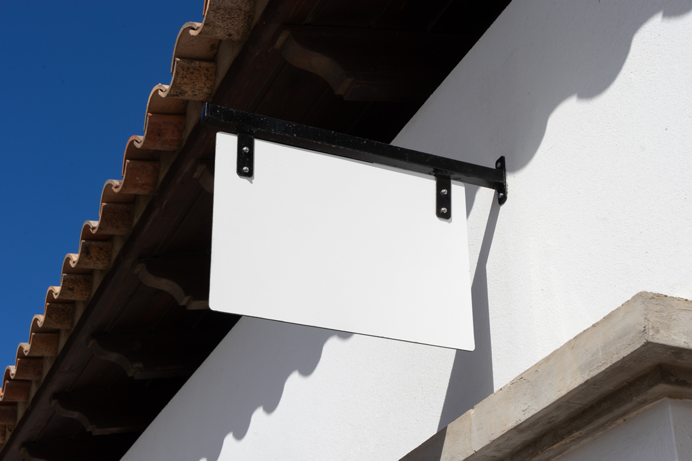 Front view, white sign mockup attached to black metal construction hanging in front of the buildings.