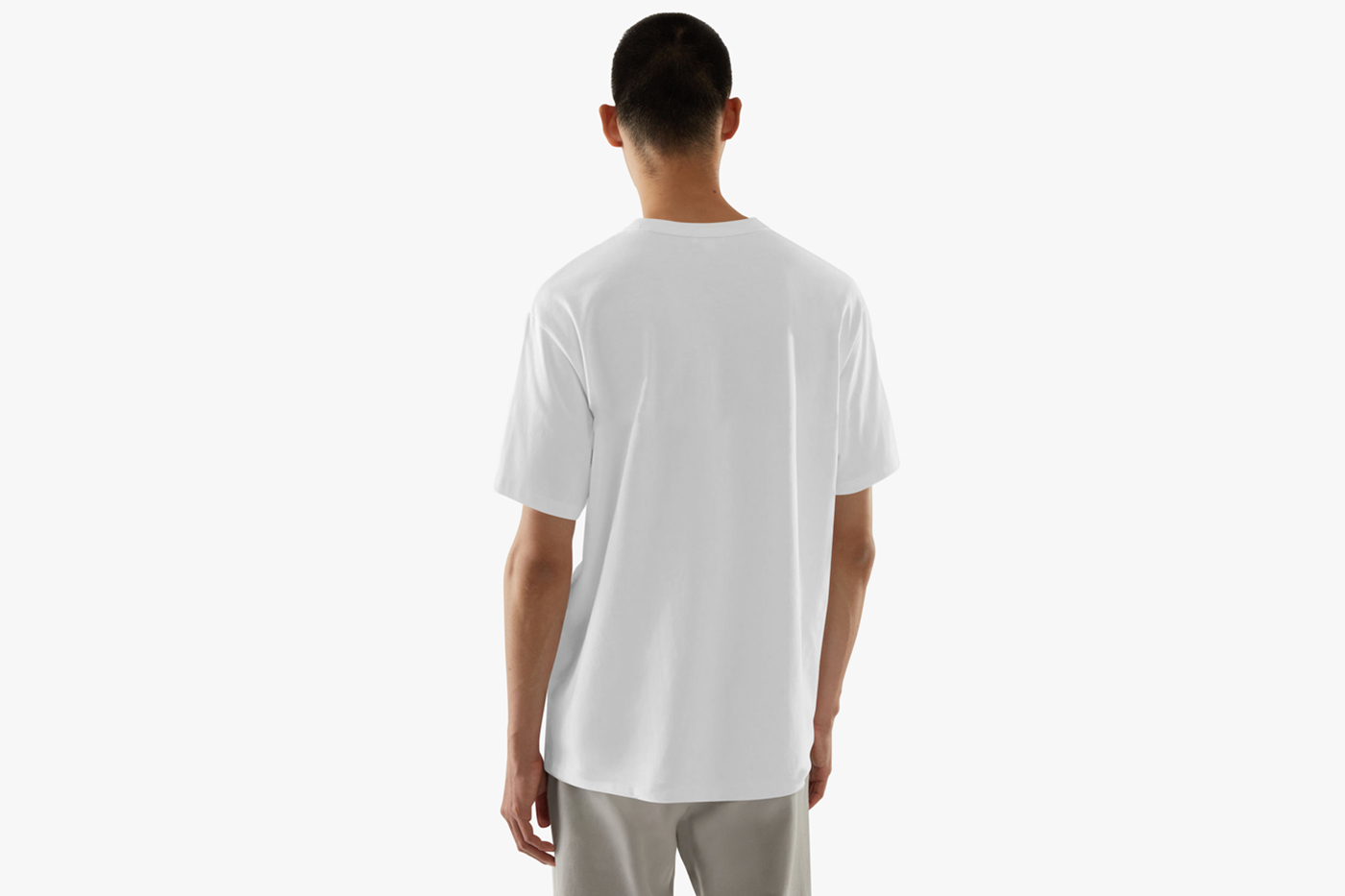 Men standing backwards wearing white t-shirt mockup in front of the white wall.