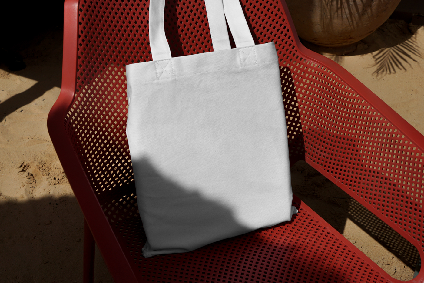 Front view, white canvas bag laying on the red plastic chair.